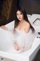 A woman in a white dress sitting in a bathtub.