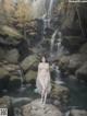 A woman in a white dress standing in front of a waterfall.