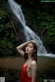 A woman in a red dress standing in front of a waterfall.