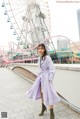 A woman in a purple coat standing in front of a ferris wheel.