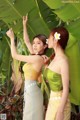 A couple of women standing next to each other near a banana tree.