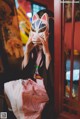 A woman in a kimono holding a cat mask over her face.